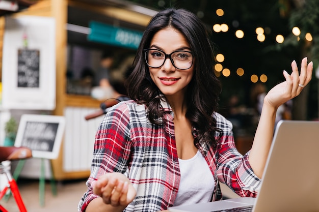 Foto gratuita hermosa chica con cabello ondulado usando computadora y sonriendo. retrato al aire libre de una dama caucásica que expresa interés durante el trabajo con la computadora portátil.