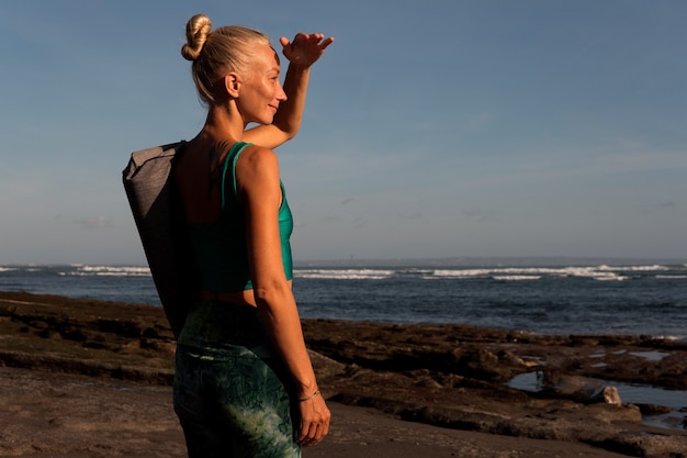 Hermosa chica caminando por la playa con estera de yoga