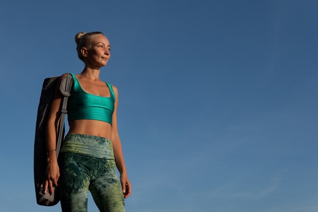 Hermosa chica caminando por la playa con estera de yoga