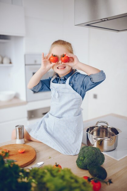 hermosa chica con una camisa azul y un delantal está preparando una ensalada de vegetales frescos en casa
