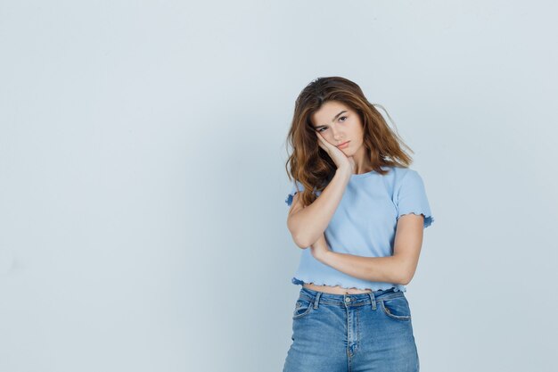 Hermosa chica en camiseta, jeans apoyando la mejilla en la palma y mirando ansiosa, vista frontal.