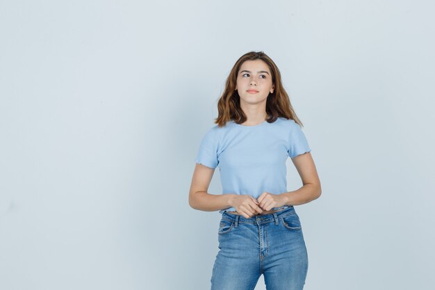 Hermosa chica en camiseta, jeans tomados de la mano frente a ella y mirando pensativo, vista frontal.