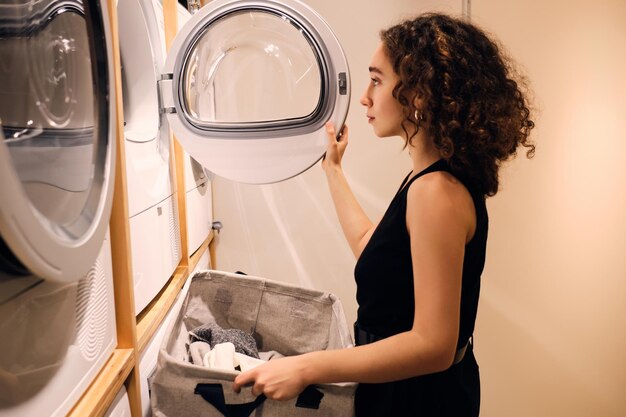 Hermosa chica cargando ropa en la lavadora en la moderna lavandería de autoservicio