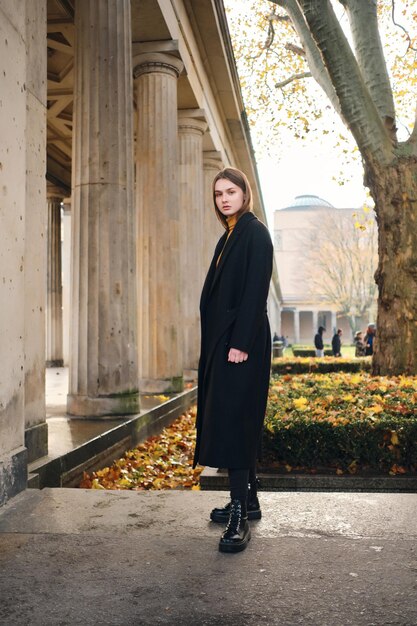 Hermosa chica casual con abrigo negro caminando cuidadosamente por el hermoso parque de la ciudad