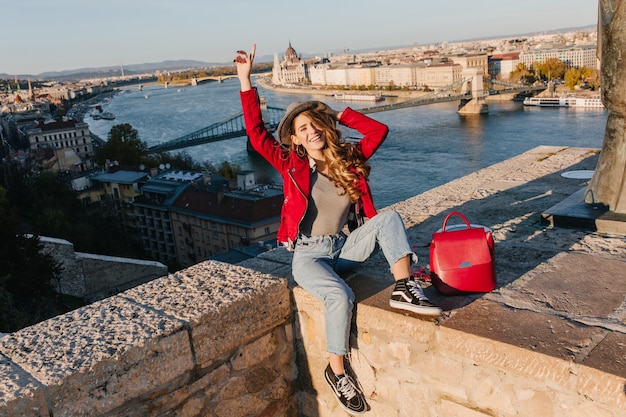 Hermosa chica en chaqueta roja de moda posando en el techo en el fondo de la ciudad