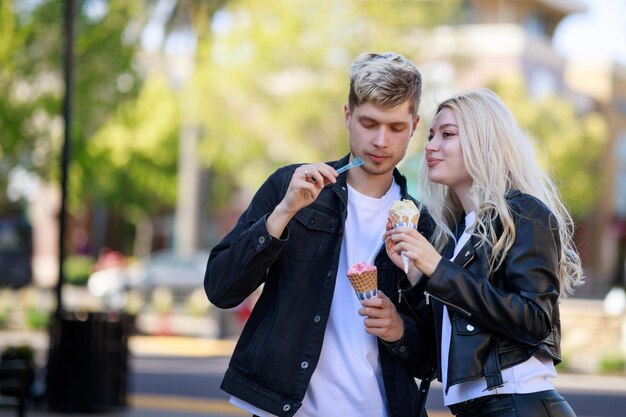 Hermosa chica y chico guapo de pie en el parque y comiendo helado