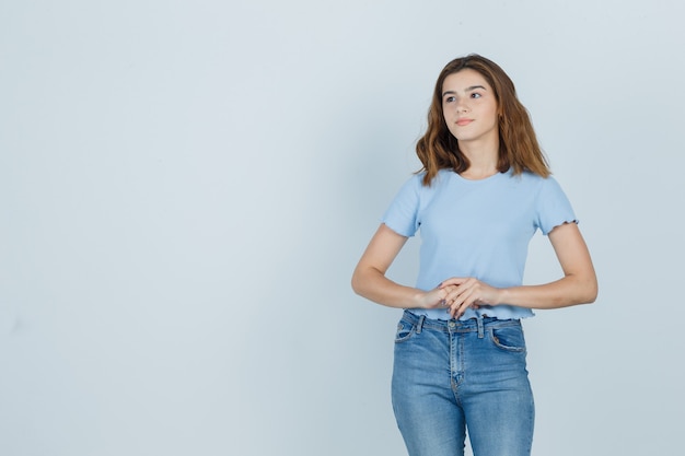 Hermosa chica cogidos de la mano frente a ella en camiseta, jeans y mirando complacido, vista frontal.