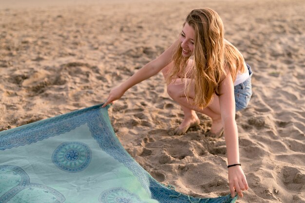 Foto gratuita hermosa chica colocando manta sobre la arena en la playa