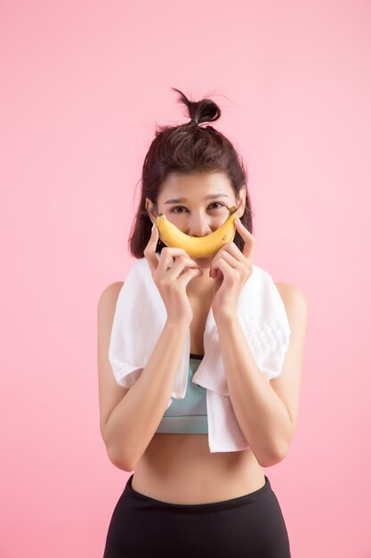 Hermosa chica comiendo bananas después de hacer ejercicio para controlar el peso.