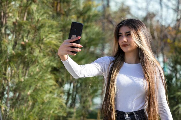 Hermosa chica confiada tomando selfie en el parque en un día soleado Foto de alta calidad