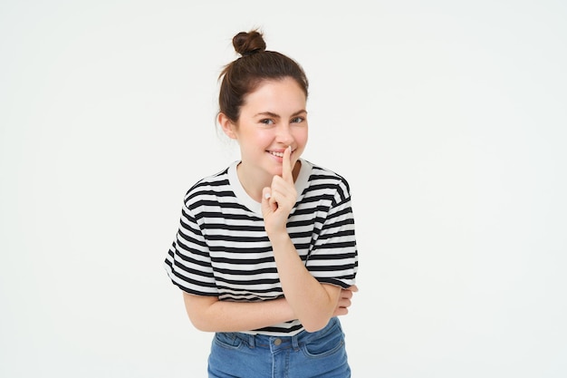 Foto gratuita una hermosa chica coqueta sostiene el dedo en los labios prometiendo mantener el secreto.