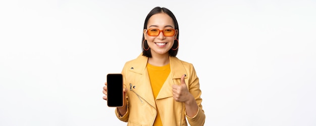 Hermosa chica coreana mujer asiática en gafas de sol que muestra la interfaz de la aplicación de teléfono inteligente pulgares arriba recomendar