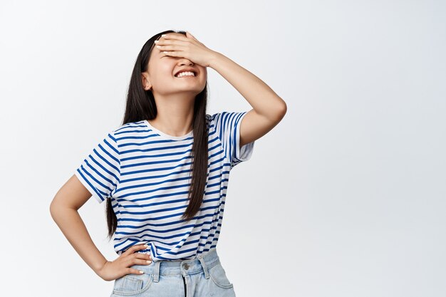 Hermosa chica coreana con ojos de sorpresa, sonriendo desde el principio, esperando algo con los ojos vendados, de pie sobre blanco.