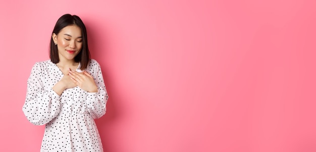 Hermosa chica coreana en vestido de primavera de moda soñando tomados de la mano en el corazón sonriendo con los ojos cerrados