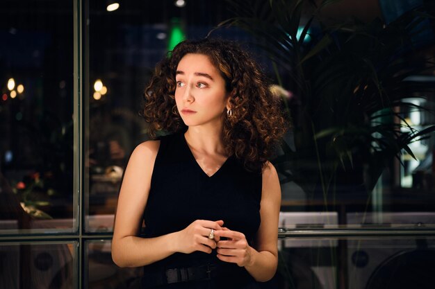 Hermosa chica cuidadosamente mirando hacia otro lado por la ventana en la moderna lavandería de autoservicio por la noche