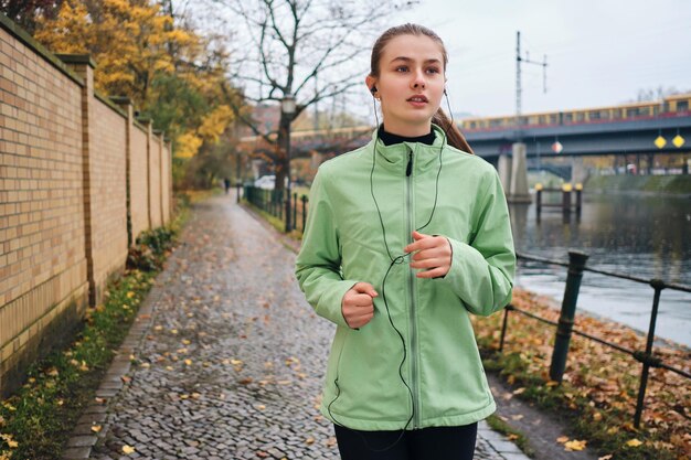 Hermosa chica deportiva en auriculares corriendo con música alrededor del parque de la ciudad