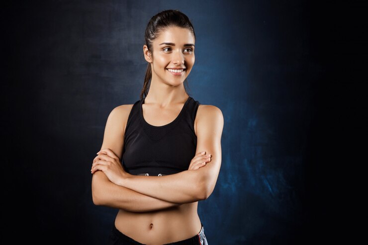 Foto gratuito hermosa chica deportiva posando con los brazos cruzados sobre la pared oscura.