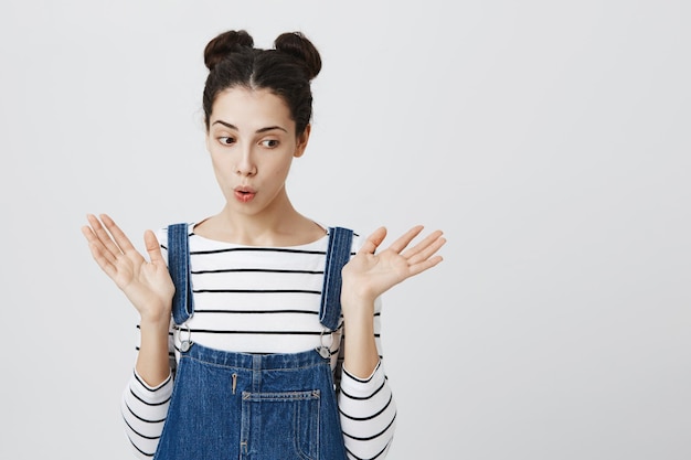 Foto gratuita hermosa chica con dos moños tiene una apariencia atractiva y atractiva y una expresión de asombro, haciendo pucheros con los labios de emoción mientras recibe noticias inesperadas.