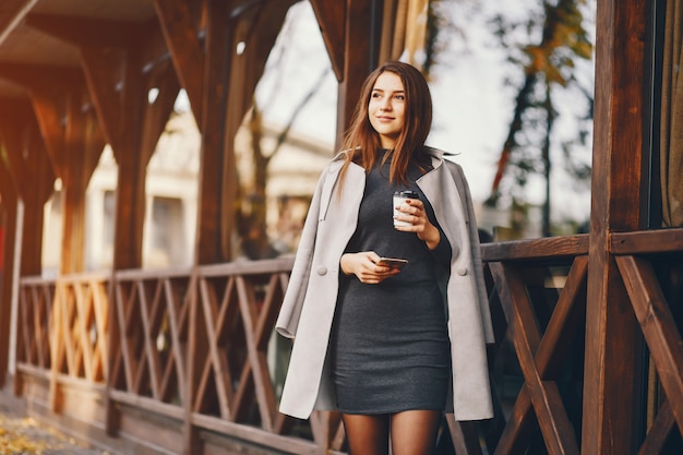 hermosa chica elegante de pie en la ciudad de otoño y beber un café