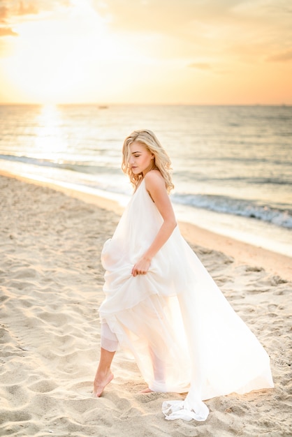 Hermosa chica elegante posando en la luz del sol en la playa