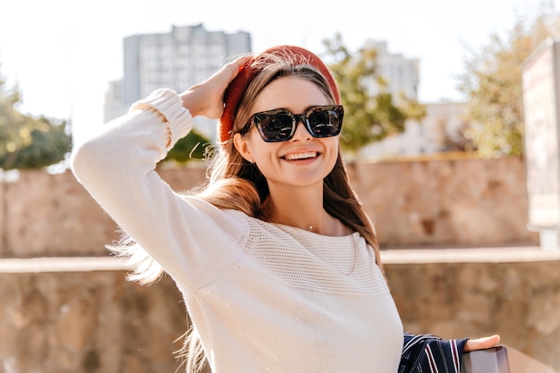 Hermosa chica elegante que expresa felicidad en el día de otoño. Foto exterior de magnífica dama blanca con boina roja.