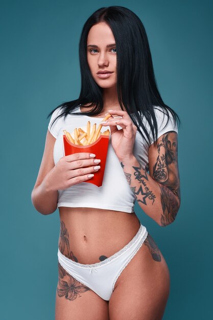 Hermosa chica encantadora del tatuaje con papas fritas