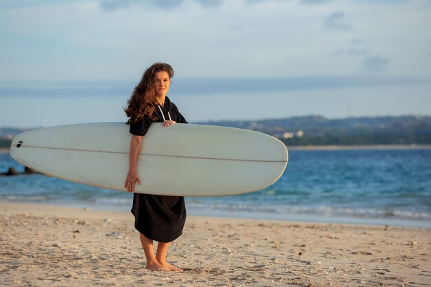 Hermosa chica se encuentra en la playa con una tabla de surf.