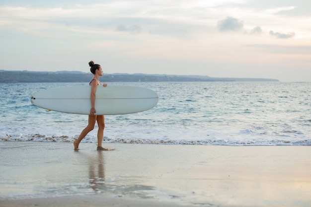 Hermosa chica se encuentra en la playa con una tabla de surf.