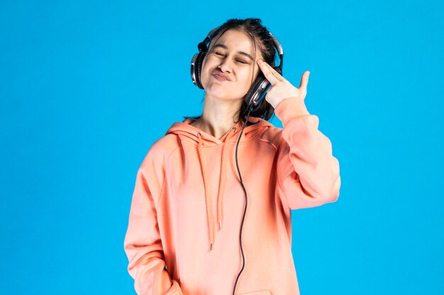 Una hermosa chica escuchando música con auriculares y apuntando su mano como un arma a su cabeza Foto de alta calidad