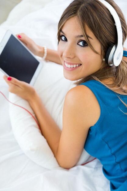 Hermosa chica escuchando música con tableta en el sofá en casa.