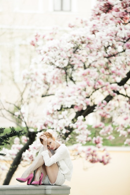 Hermosa chica está sentada en la barandilla cerca del increíble árbol de magnolia