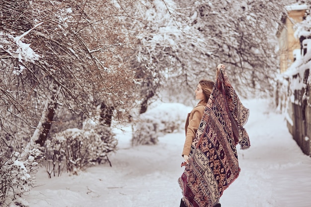 Hermosa chica está sosteniendo una bufanda revoloteando en un parque de invierno