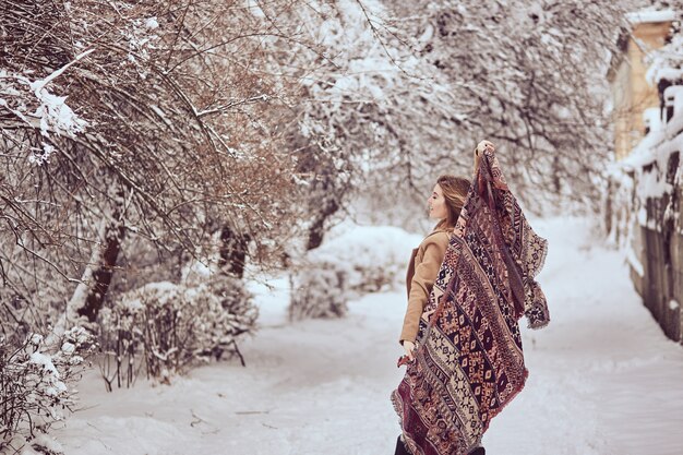 Hermosa chica está sosteniendo una bufanda revoloteando en un parque de invierno