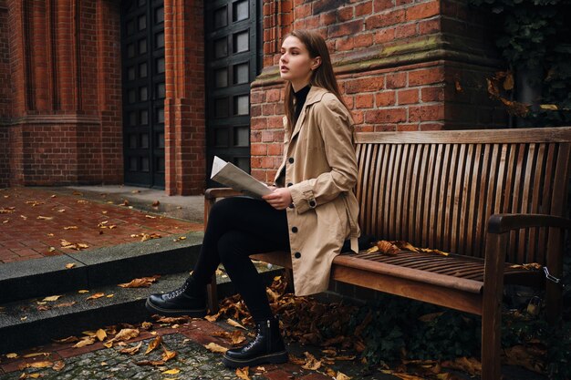 Hermosa chica con estilo mirando con confianza hacia otro lado leyendo el periódico en un banco al aire libre