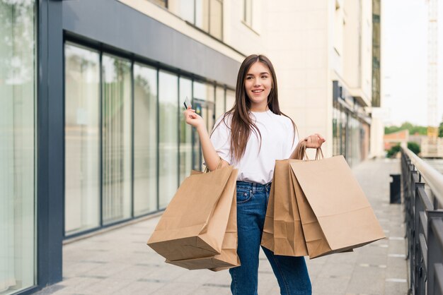 Hermosa chica en gafas de sol sostiene bolsas de la compra y sonríe mientras camina por la calle