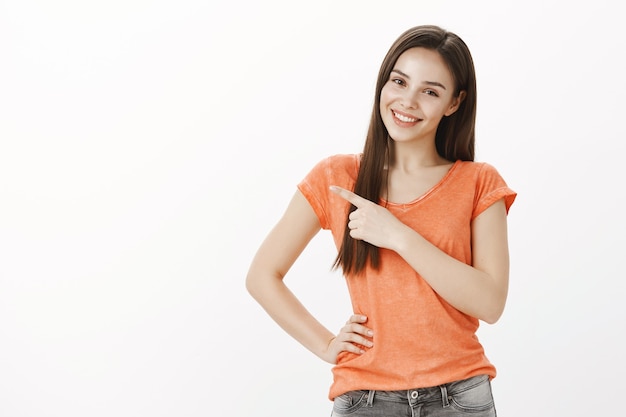 Hermosa chica glamour sonriente, señalando la esquina superior izquierda del dedo, demuestra banner y promoción