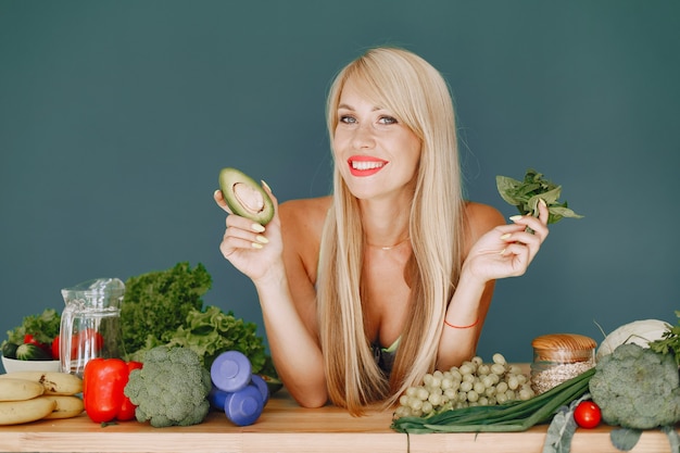 Hermosa chica hace una ensalada. Rubia deportiva en una cocina. Mujer con aguacate.