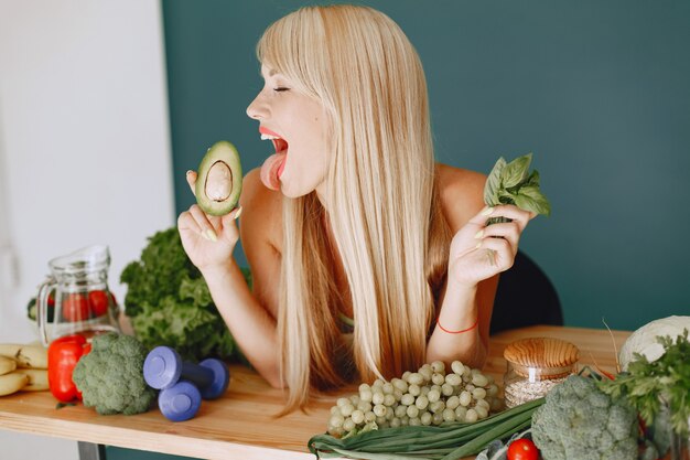 Hermosa chica hace una ensalada. Rubia deportiva en una cocina. Mujer con aguacate.