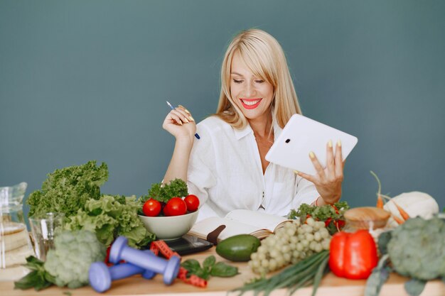 Hermosa chica hace una ensalada. Rubia deportiva en una cocina. Receta de escritura de mujer en el cuaderno.