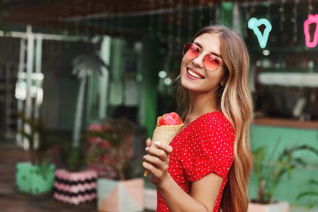 Hermosa chica hipster en gafas de sol comiendo helado y sonriendo