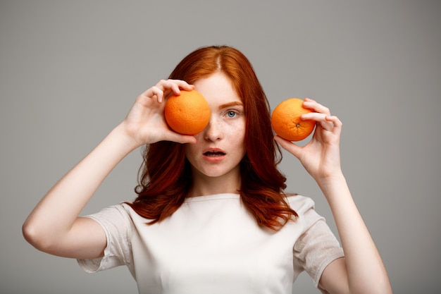 Hermosa chica de jengibre con naranjas sobre pared gris.