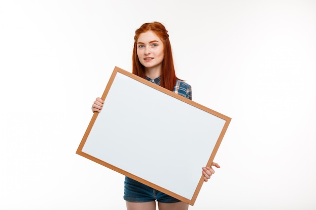 Hermosa chica de jengibre con pizarra sobre pared blanca.