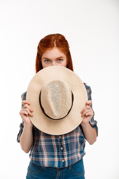 Hermosa chica de jengibre con sombrero sobre pared blanca.