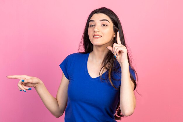 Una hermosa chica levantó el dedo y miró la cámara y el fondo rosa.