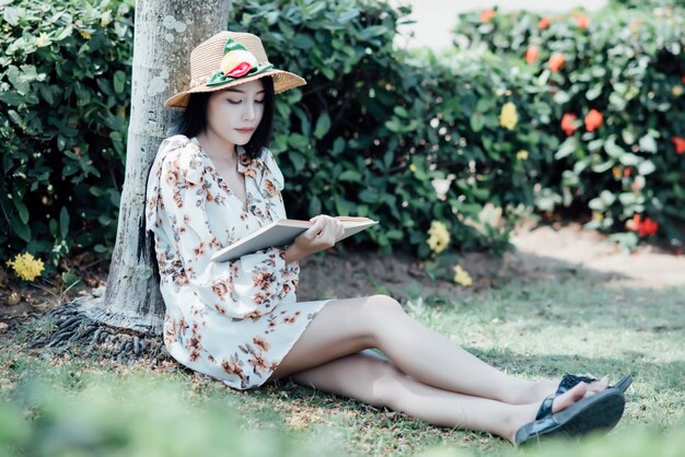 Hermosa chica leyendo un libro en el parque en la luz del sol de verano