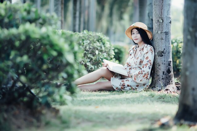 Hermosa chica leyendo un libro en el parque en la luz del sol de verano