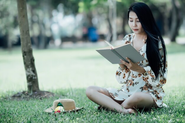 Hermosa chica leyendo un libro en el parque en la luz del sol de verano