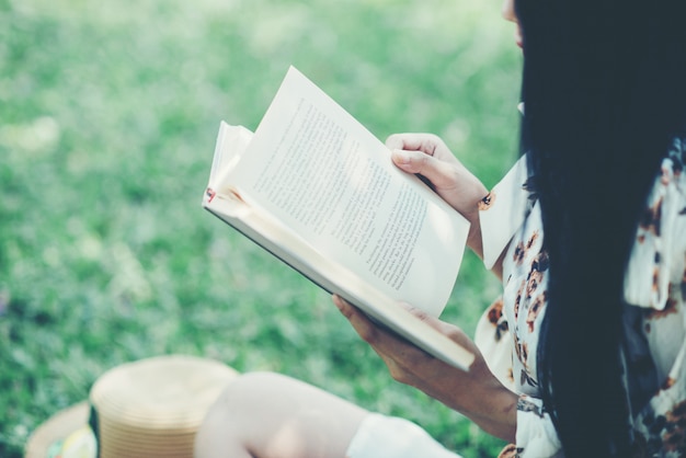 Hermosa chica leyendo un libro en el parque en la luz del sol de verano