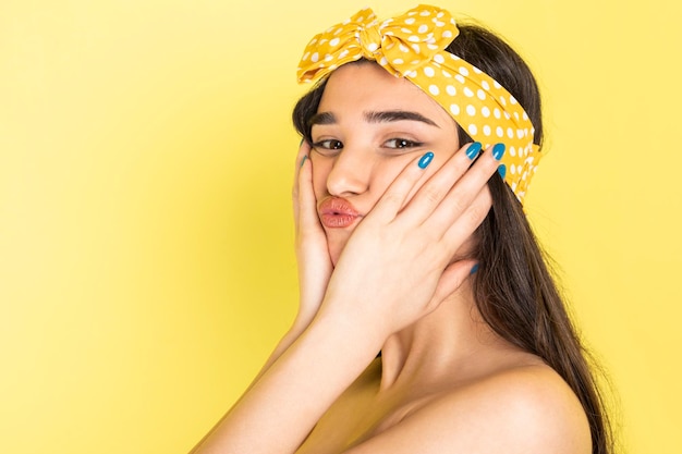 Hermosa chica llevándose las manos a la cara y de pie sobre fondo amarillo Foto de alta calidad