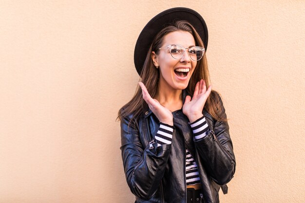 Hermosa chica de moda feliz en chaqueta de cuero y sombrero negro aislado en la pared de color amarillo claro